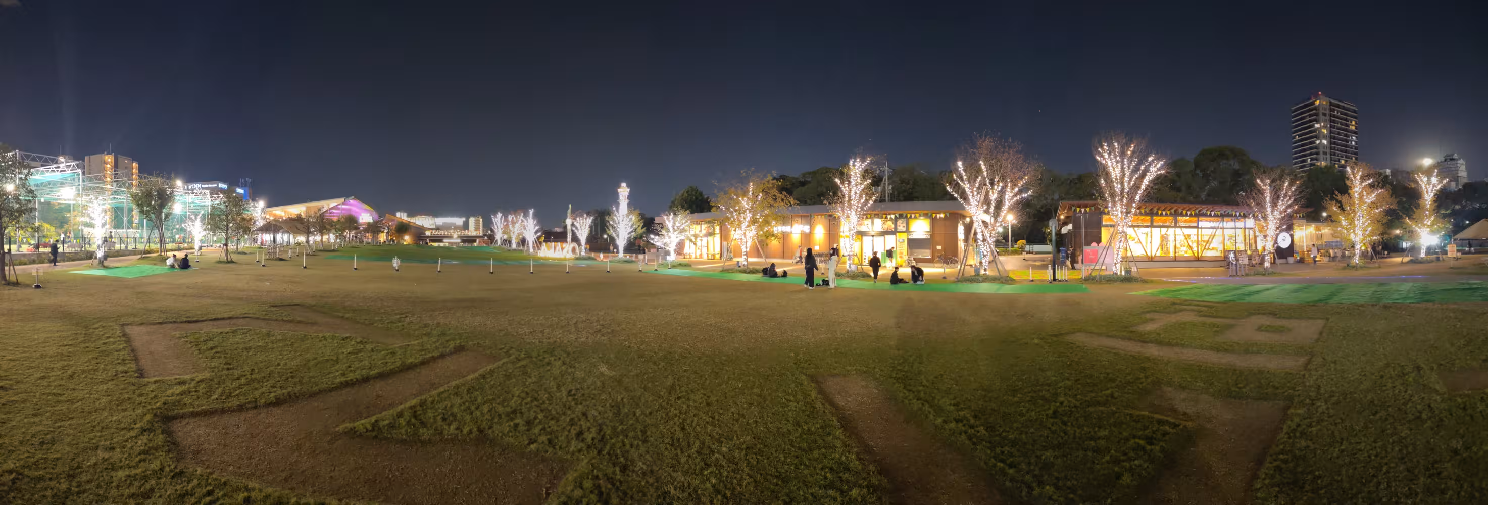 A green square in Osaka with surrounded by lit up trees.
