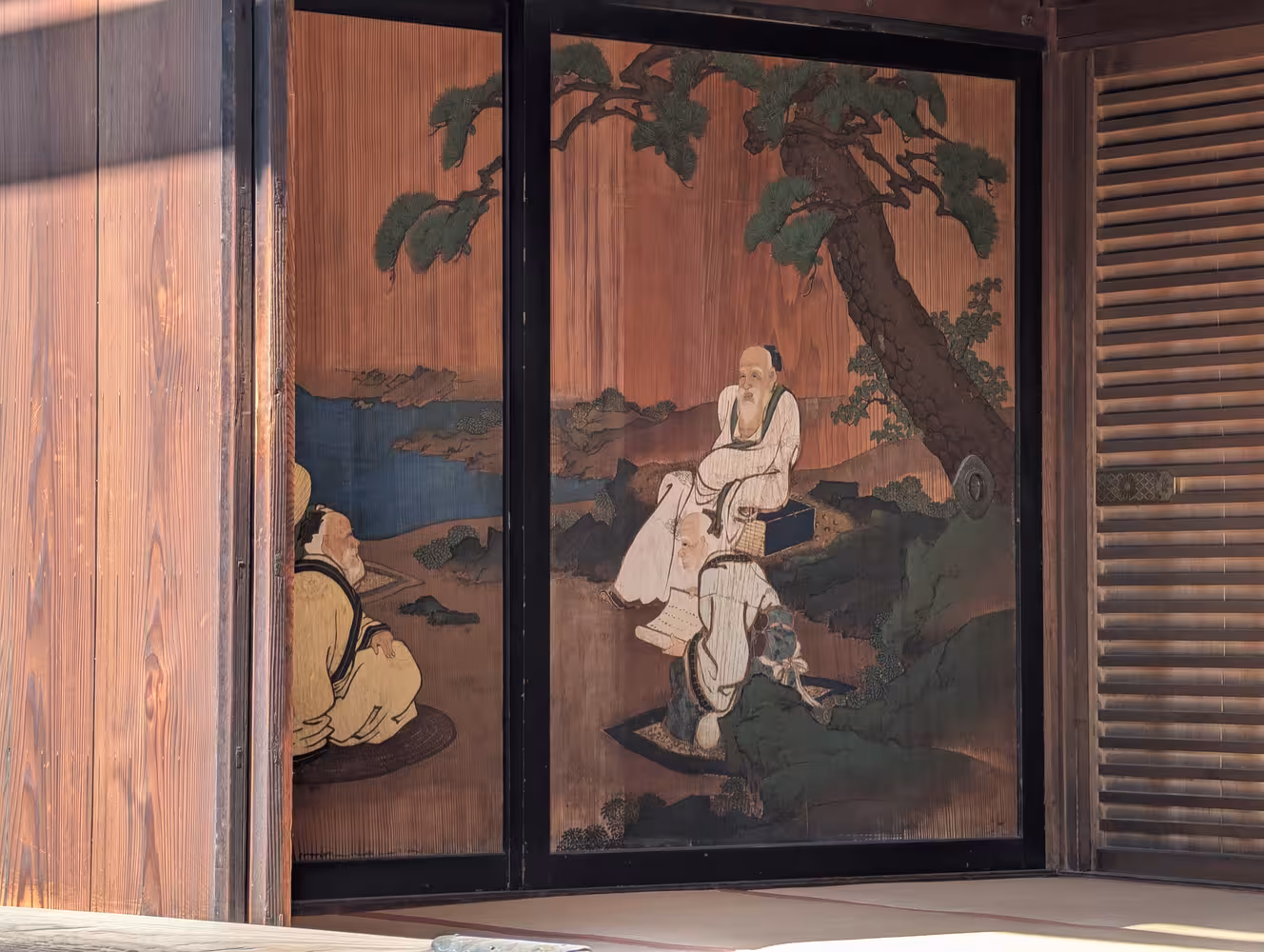 An internal wooden door with a painting of men sitting under a tree on it.