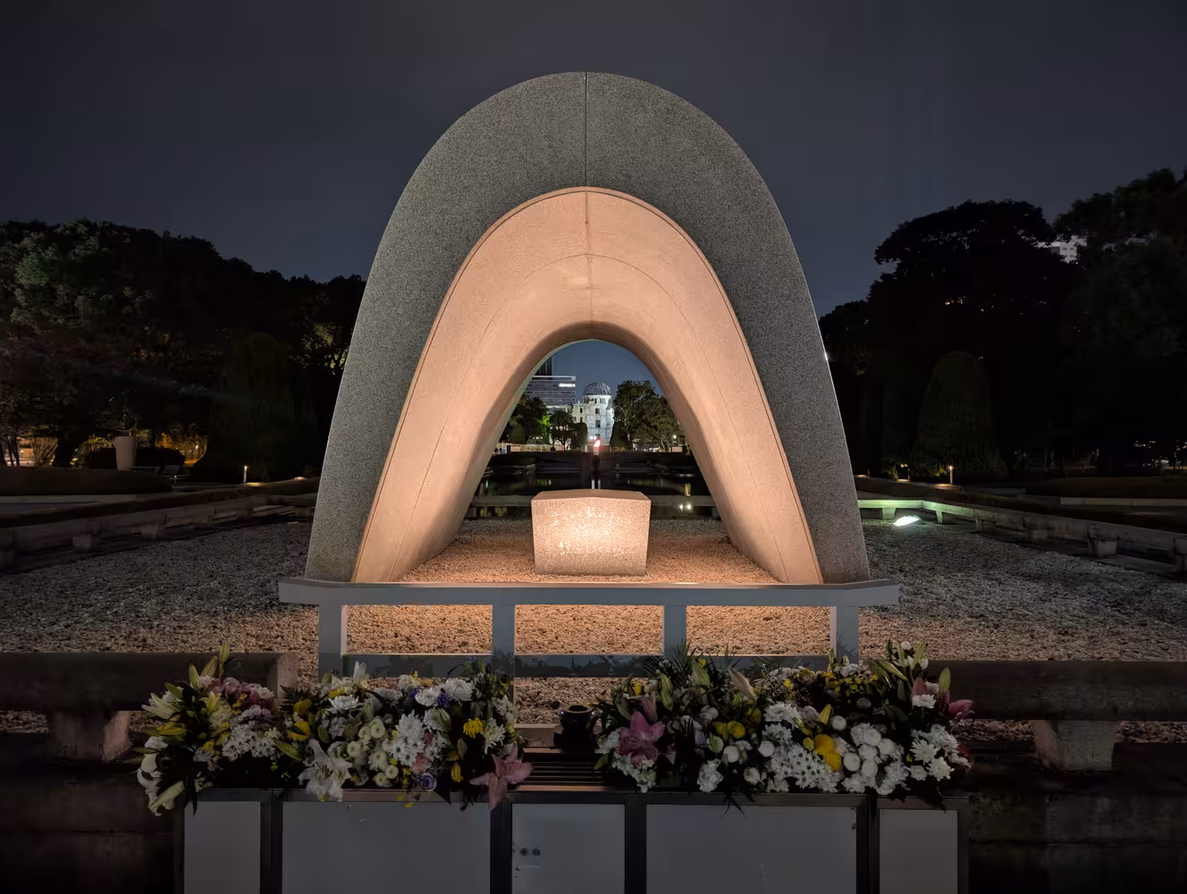 A shrine in front of a stone altar below a concrete arch at night. The atomic bomb dome is visible through it.