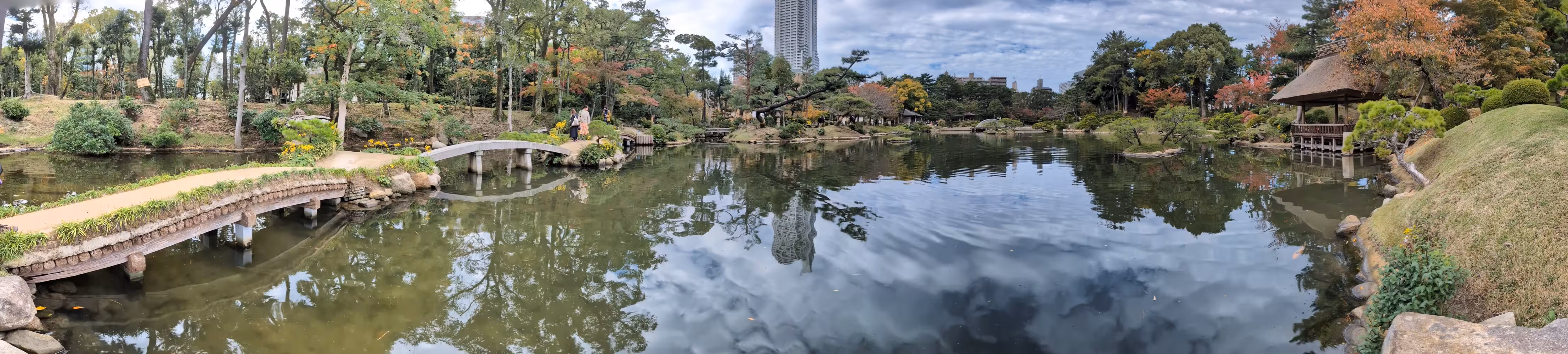 panorama view of the lake, surrounded by trees, hills, a shelter, bridges and walkways.